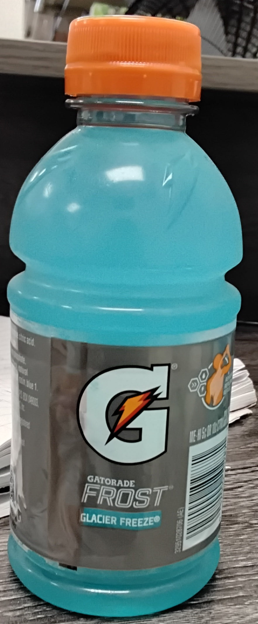 A 12 oz bottle of TOJ EXPRESS Gatorade Glacier Freeze with an orange cap rests on a dark wooden surface, displaying the Gatorade logo and nutritional info on its label.