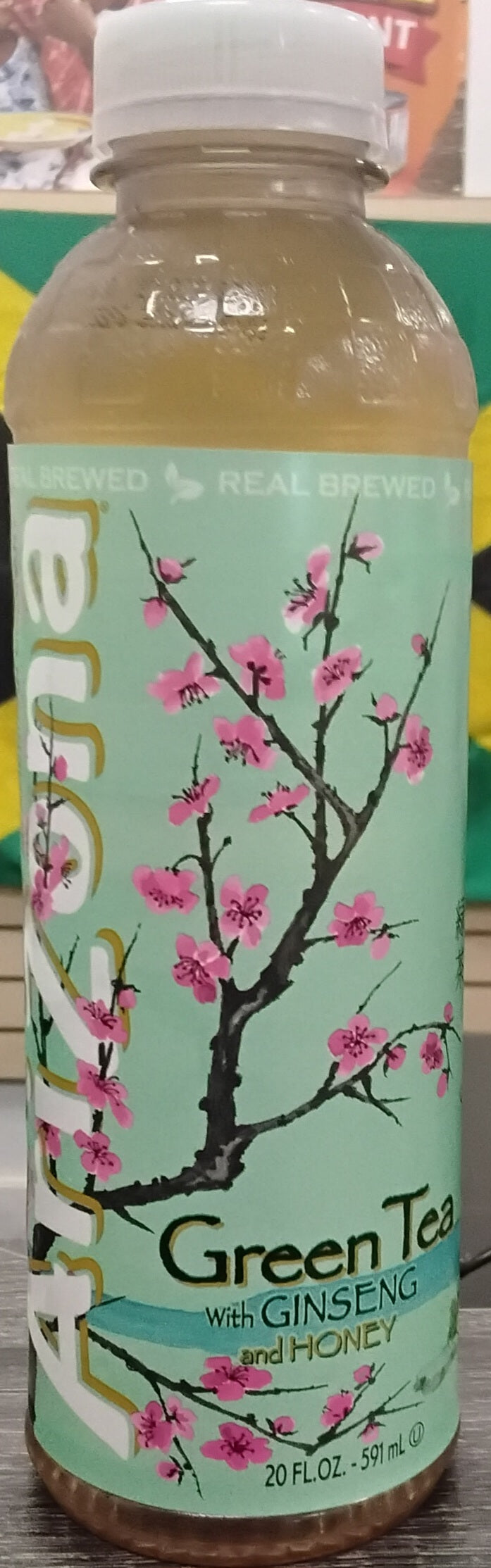 A bottle of TOJ EXPRESS Arizona Green Tea, known for antioxidants, stands upright on a counter with a light green label, pink cherry blossoms, and bold white text.
