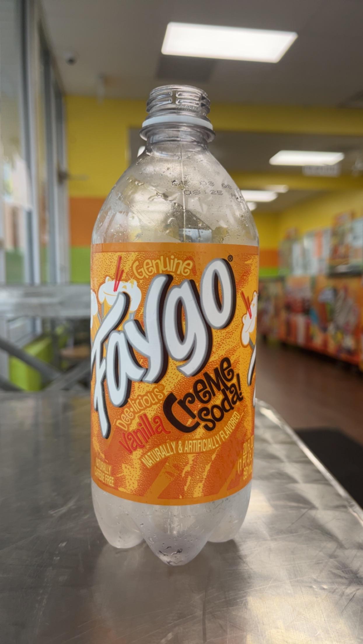 A partially empty 20 oz Faygo Creme Soda from TOJ EXPRESS rests on a metal table in a brightly lit store with colorful walls and large windows.