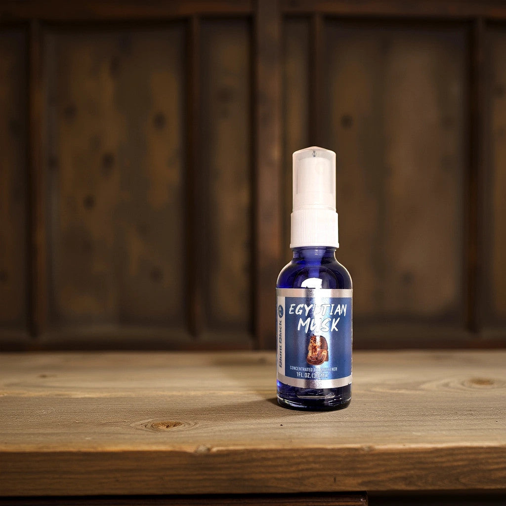 A blue bottle of BlackBlunt_Egyptian Musk massage oil by TOJ EXPRESS sits on a wooden surface, emitting a scent similar to a high-end air freshener, with a blurred rustic wooden panel in the background.