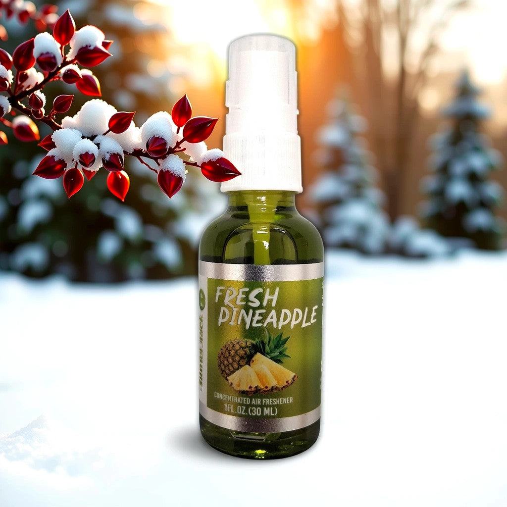 The Blunt Black Air Freshener-Pineapple by TOJ EXPRESS is a small spray bottle labeled Fresh Pineapple, adorned with pineapple images. It stands on snow next to red and white leaves, set against a blurred forest backdrop in warm light.