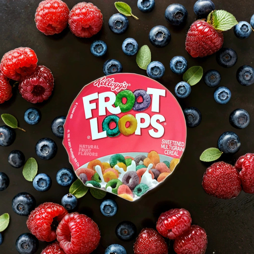 A 1.5oz cup of TOJ EXPRESS Kellogg's Froot Loops is surrounded by fresh blueberries, raspberries, and green leaves, all artfully arranged on a dark surface.