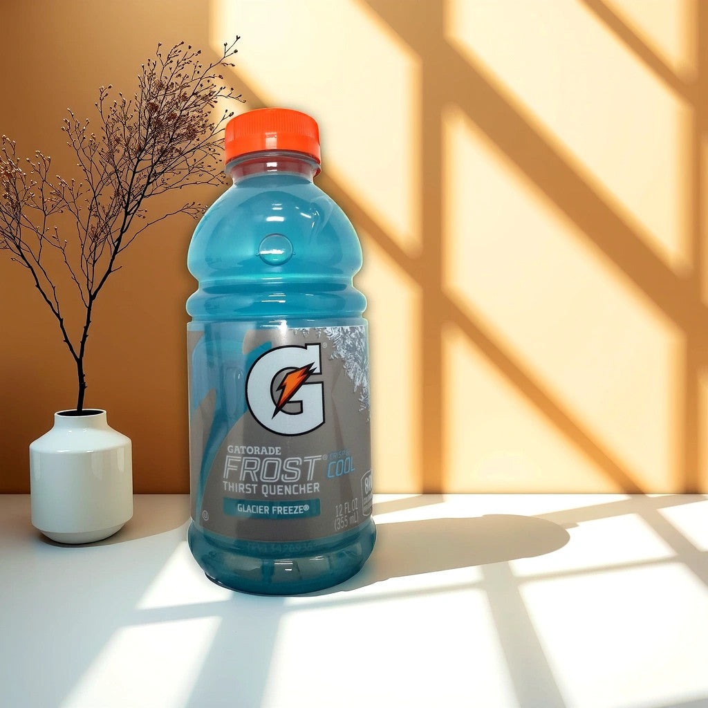 A 12 oz Gatorade Frost Drink by TOJ EXPRESS labeled Frost Glacier Freeze rests on a white surface, complemented by a small white vase with a branch against a beige wall with lattice shadows, creating an artistic backdrop for this hydration solution.