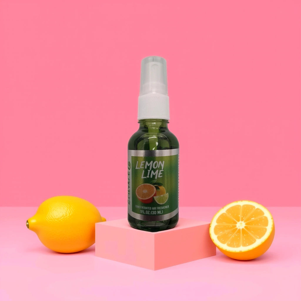 A lemon and half lemon rest beside a green spray bottle labeled Blunt Black Air Freshener-Lemon Lime from TOJ EXPRESS. Set against a vibrant pink background, the white nozzle spritzes a refreshing scent, all perched on a light pink block.