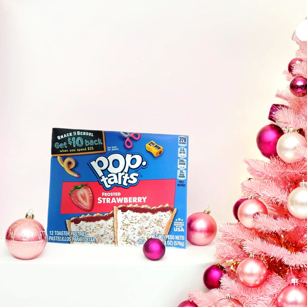 A box of TOJ EXPRESS Pop Tarts-Frosted Strawberry rests on a white surface beside a pink Christmas tree with matching ornaments—an ideal festive, portable snack. Pink ornaments are scattered around the strawberry pastry box.