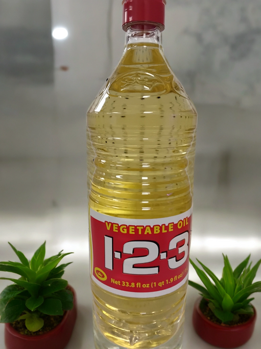 A clear plastic bottle of TOJ EXPRESS 123Vegetable Cooking Oil with a red and yellow label stands upright between two small potted green succulents on a reflective surface.