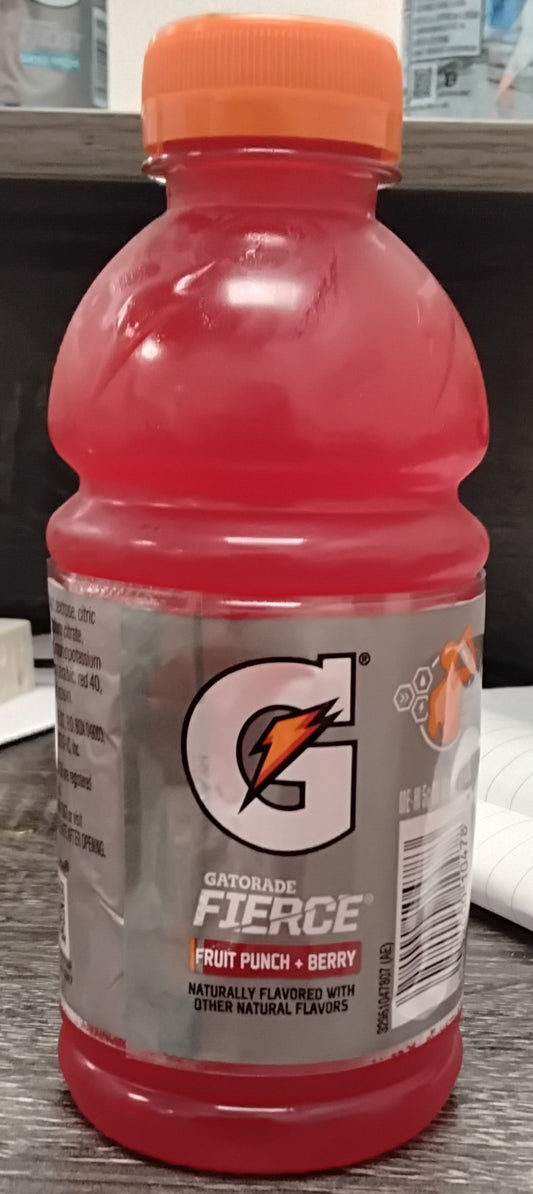A 12 oz bottle of TOJ EXPRESS Gatorade Fruit Punch + Berry with an orange cap sits on a desk, showing the Gatorade logo and product info. A notebook and other items are visible in the background.