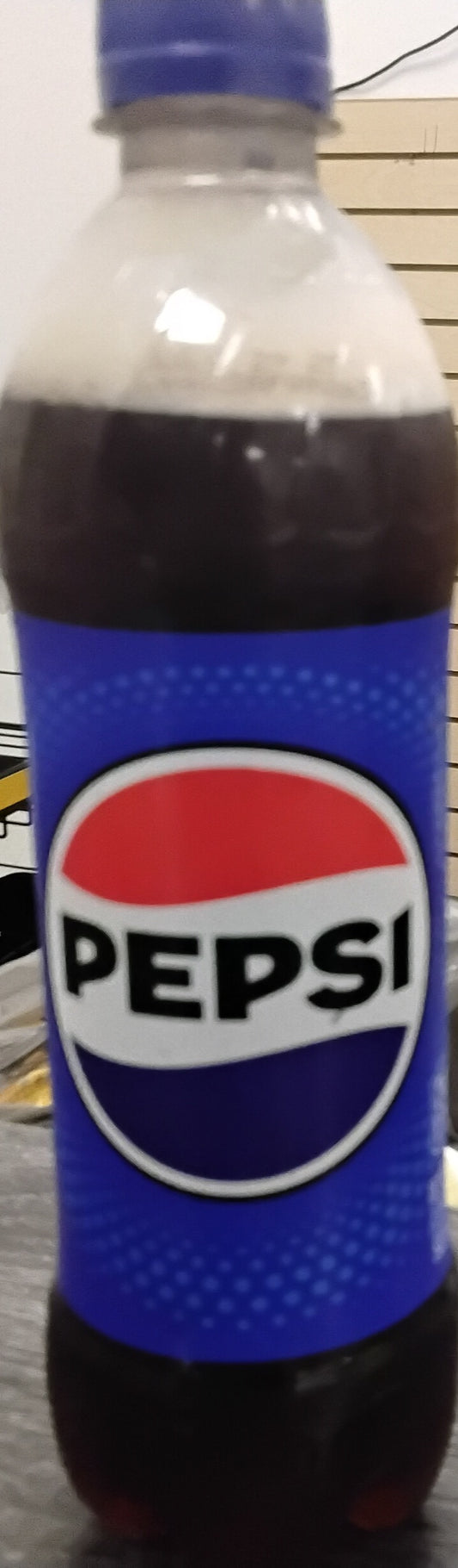 A 16.9 fl oz bottle of Pepsi Soda with caffeine from TOJ EXPRESS, featuring a blue label and cap with the classic red, white, and blue logo, sits indoors—a refreshing drink for any occasion.