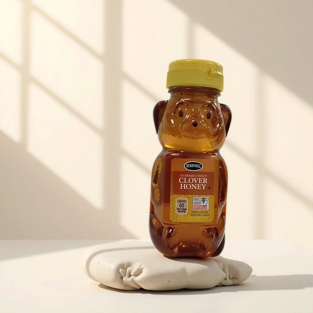 A bear-shaped plastic bottle of TOJ EXPRESS BerryHill Clover Honey with a yellow cap rests on a soft white surface, sunlight streaming through a window and casting shadows—golden sweetness in nature-inspired form.