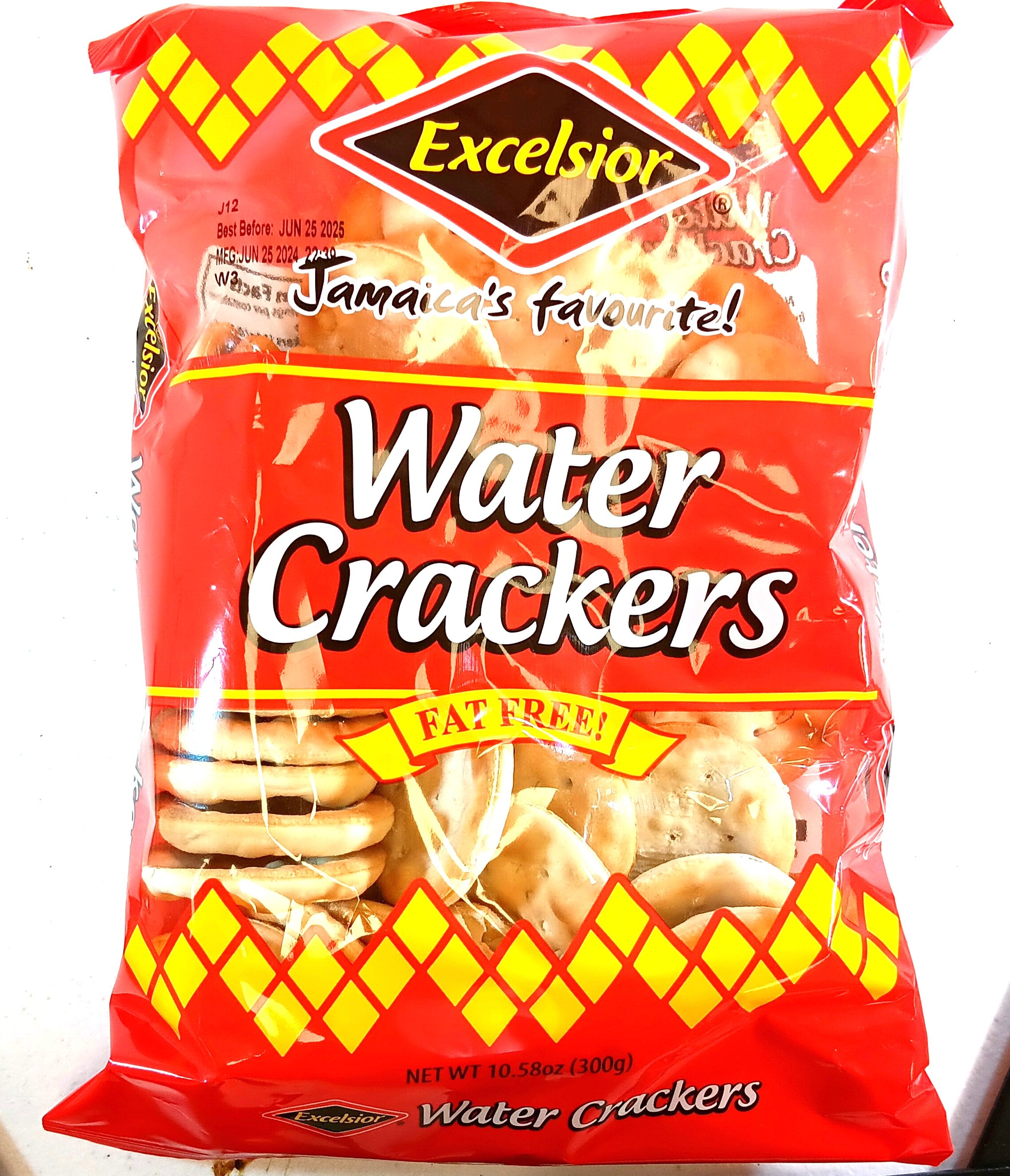 The image shows a red TOJ EXPRESS Excelsior Water Crackers bag, with Jamaicas favourite! and Fat Free! labels. Made from top-quality ingredients, these 10.58 oz (300g) crispy crackers come in packaging adorned with yellow diamond patterns and a clear window displaying the crackers.