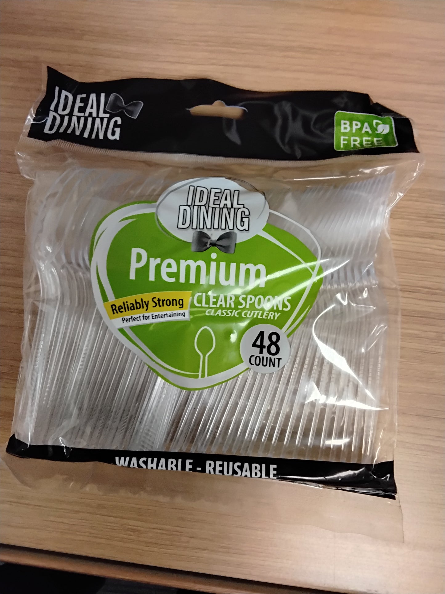 A package of 48 TOJ EXPRESS Ideal Dining Clear Spoons rests on a wooden surface, showcasing reliably strong, BPA-free, washable, and reusable spoons—perfect for any occasion.