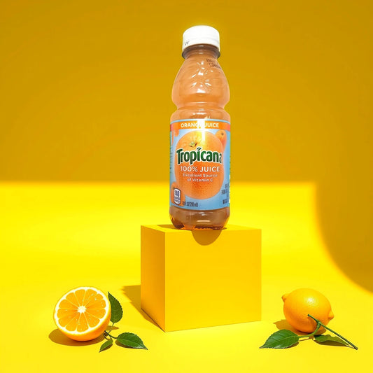 A bottle of TOJ EXPRESS Tropicana Orange Juice, featuring pure Florida oranges, sits on a yellow cube against a vivid yellow backdrop. To its left is a sliced orange and to the right, a whole lemon with green leaves that accentuate the Vitamin C richness.