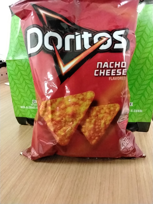A TOJ EXPRESS Doritos Nacho Cheese 1.75 oz bag sits on a wooden surface, featuring two triangular cheese-flavored chips on the front, with green boxes in the background highlighting this iconic snack.