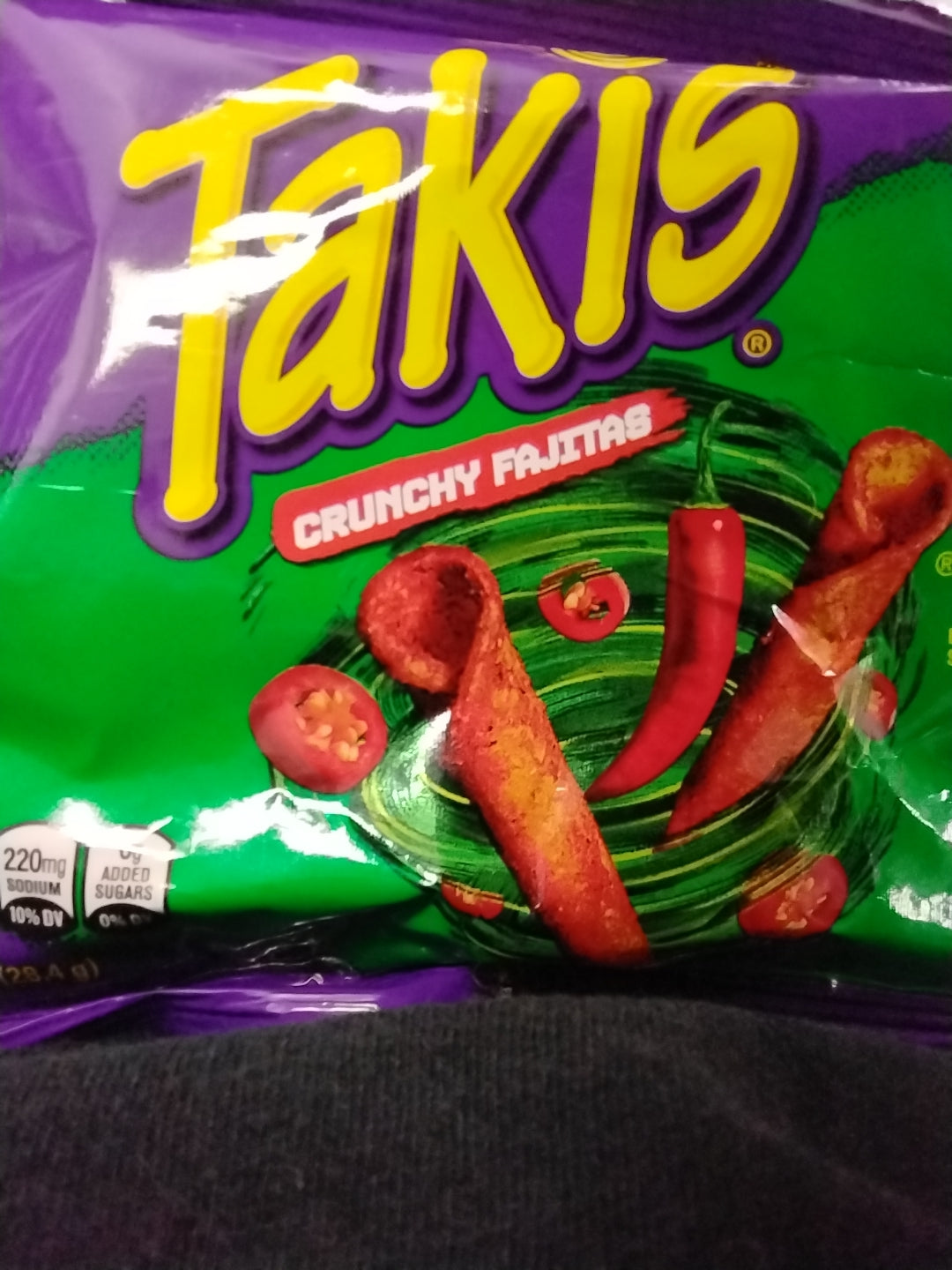 A 1 oz bag of TOJ EXPRESS Takis - Crunchy Fajitas, a savory rolled chip snack with chili peppers and jalapeño slices, shown on a green and purple background with nutrition facts like calories and added sugars displayed on the front.