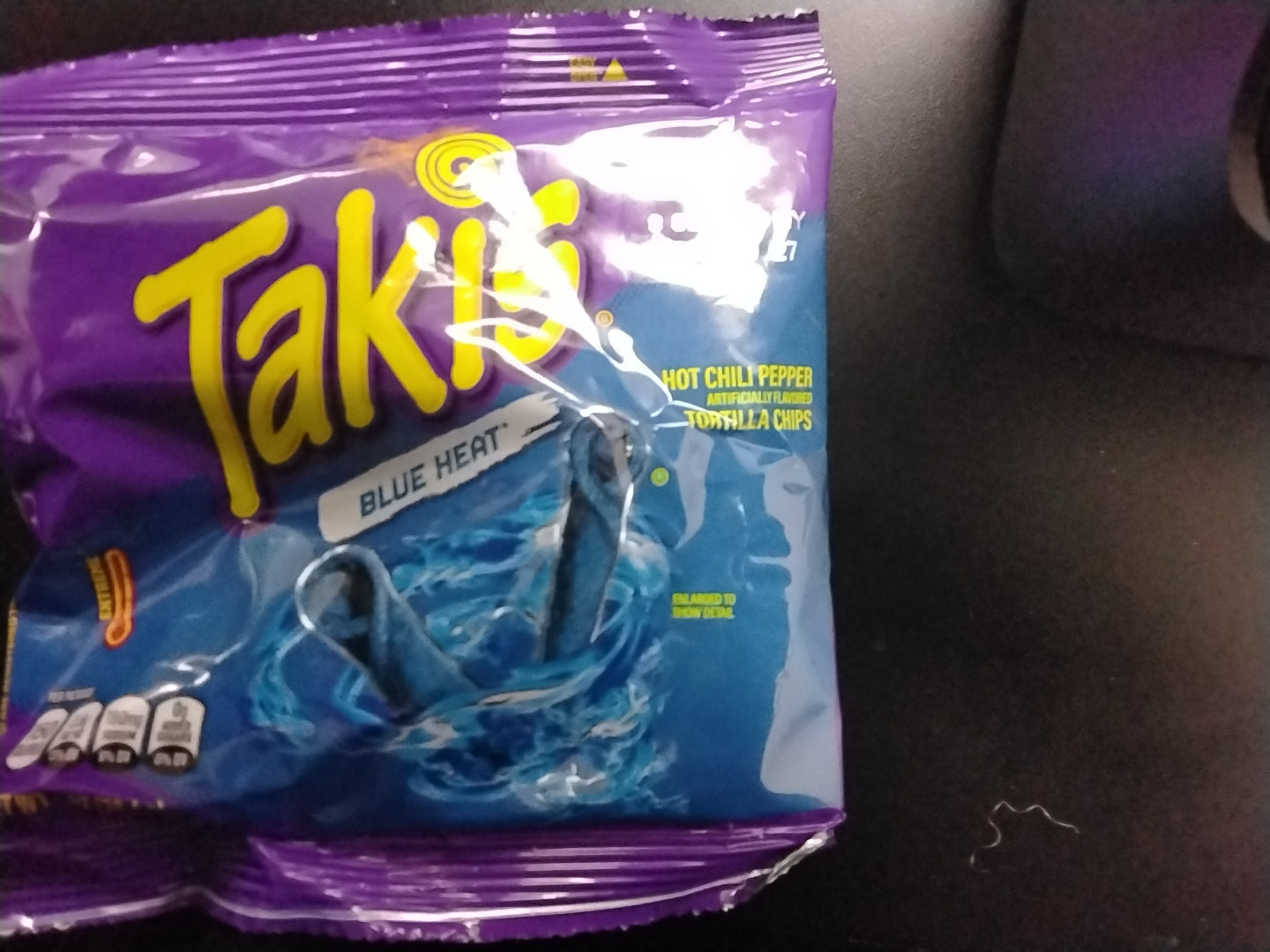 A bag of TOJ EXPRESS Takis - Blue Heat is displayed on a dark surface, with its purple packaging featuring bold blue rolled chips and flames, emphasizing this intense spicy snack.