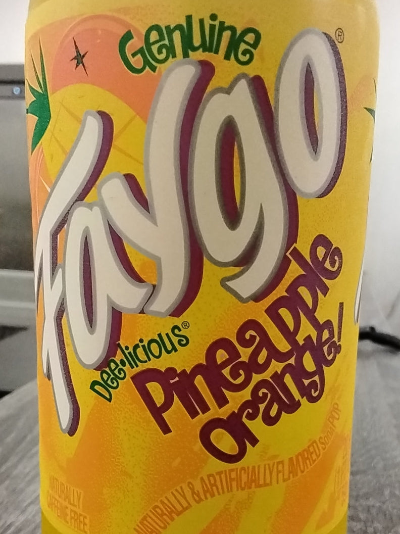 Close-up of a 20oz Faygo Pineapple Orange Soft Drink by TOJ EXPRESS, featuring bold text and images of pineapples and oranges on a yellow background with the words Genuine, Delicious, Naturally & Artificially Flavored visible.